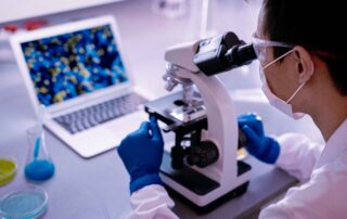 Woman looking through a microscope with a computer in front of her to review data.