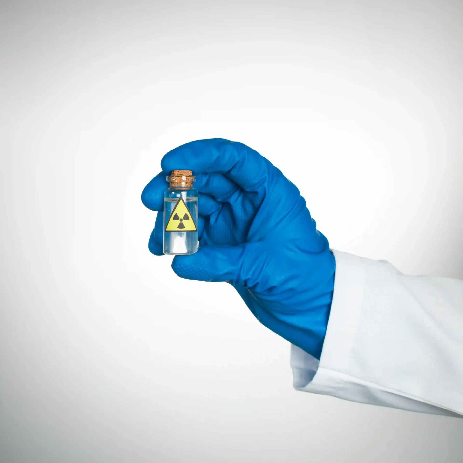 hand with blue medical glove holding a small glass vile with radioactive icon on it