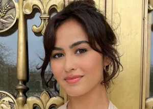 Head-and-shoulders portrait of a woman with dark hair and subtle makeup, standing in front of an ornate gold door.