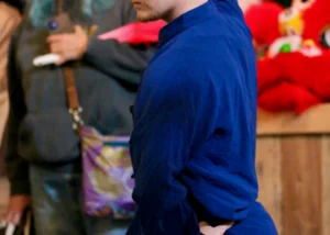 Man in a blue martial-arts uniform in a low stance, performing a move, with onlookers watching in the background.
