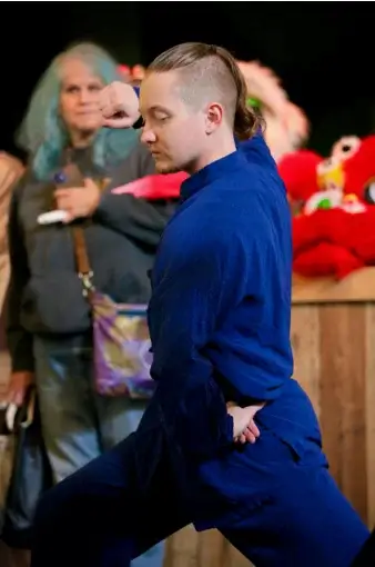 Man in a blue martial-arts uniform in a low stance, performing a move, with onlookers watching in the background.
