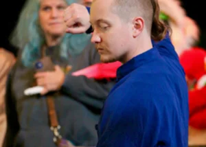 Man in a blue shirt seen in profile at a crowded event, with people blurred in the background.