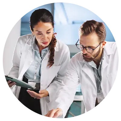 Two researchers in white lab coats review data on a tablet in a laboratory environment.